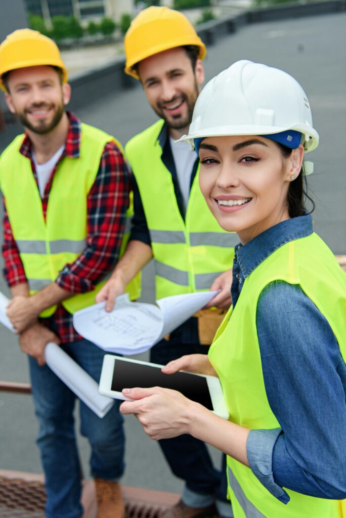 architects in safety vests and hardhats working with digital tablet and blueprints